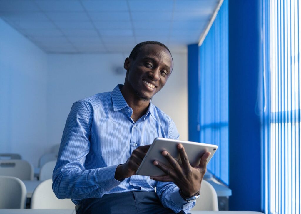 A smiling adult man using a tablet in a brightly lit office space.