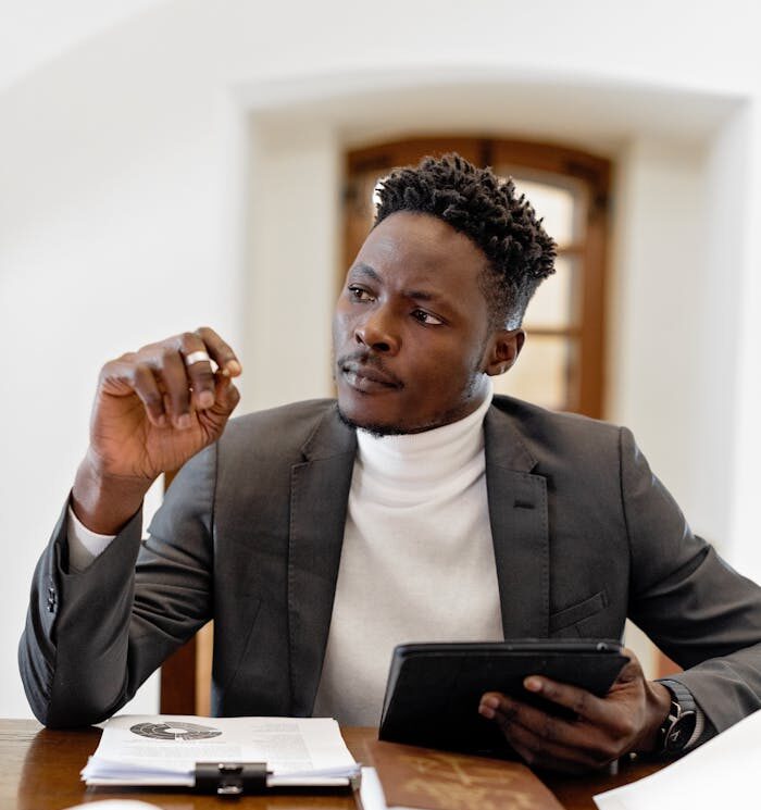 Confident black male professional in office setting consulting a tablet.